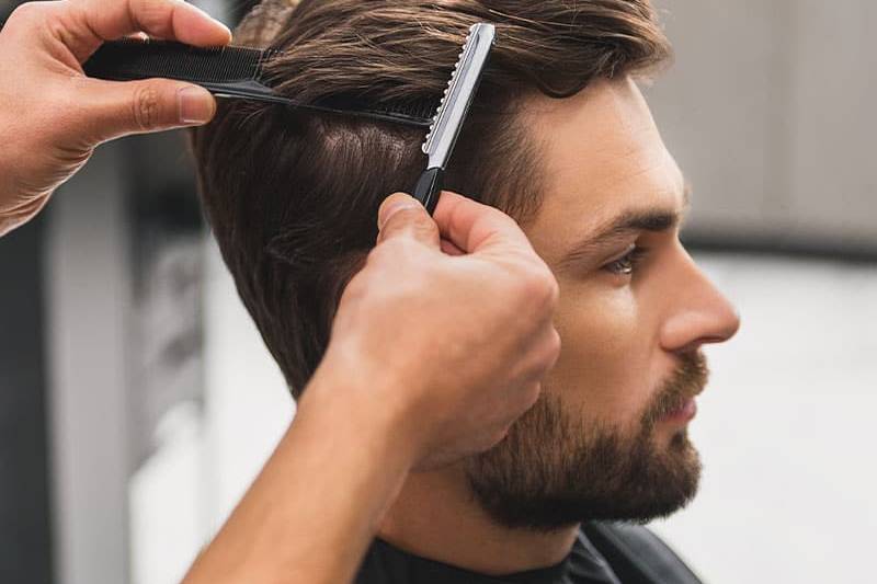 Dunkelblonder Mann erhält lockere Kurzhaarfrisur mit Kamm und Rasiermesser.