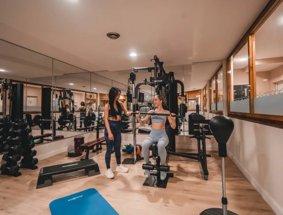 Zwei Damen trainieren im Fitnessraum des Arkona Strandhotels Binz auf Rügen mit Kraftgeräten, Hanteln und Spiegeln