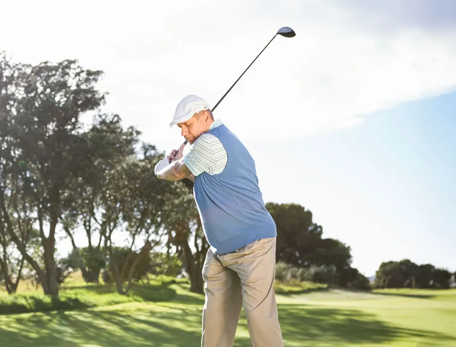 Ein Golfspieler schlägt einen Ball ab, im Hintergrund ein sonniger Golfplatz.