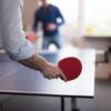 Aufnahme eines Mannes beim Tischtennis spielen von hinten, den roten Schläger in der Hand.