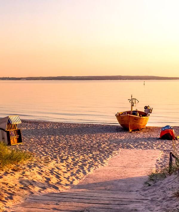 Ein hölzernes Boot liegt im Sonnenuntergang am Strand, daneben zwei Strandkörbe.