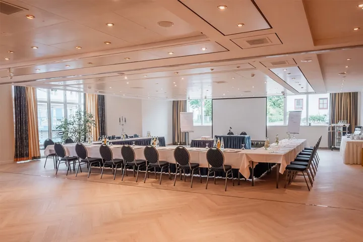 Conference room with U-shaped seating, projector screen, large windows and modern lighting at the Arkona Strandhotel in Binz.