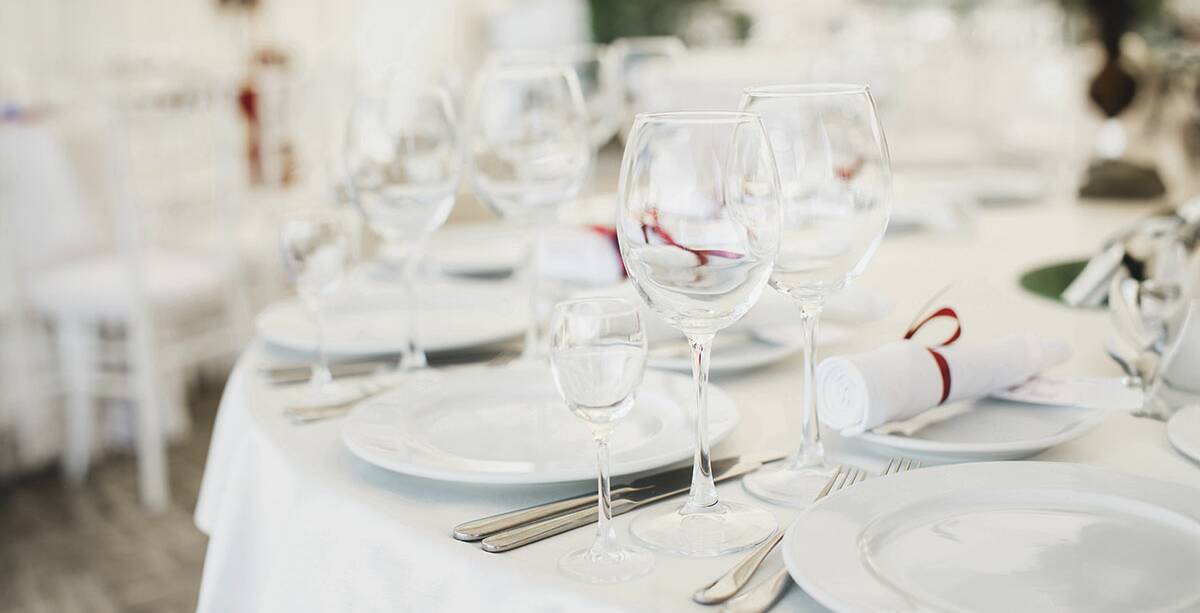 Ein elegant eingedeckter weißer Tisch mit jeweils drei verschiedenen Gläsern neben den Tellern