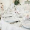 Ein elegant eingedeckter weißer Tisch mit jeweils drei verschiedenen Gläsern neben den Tellern