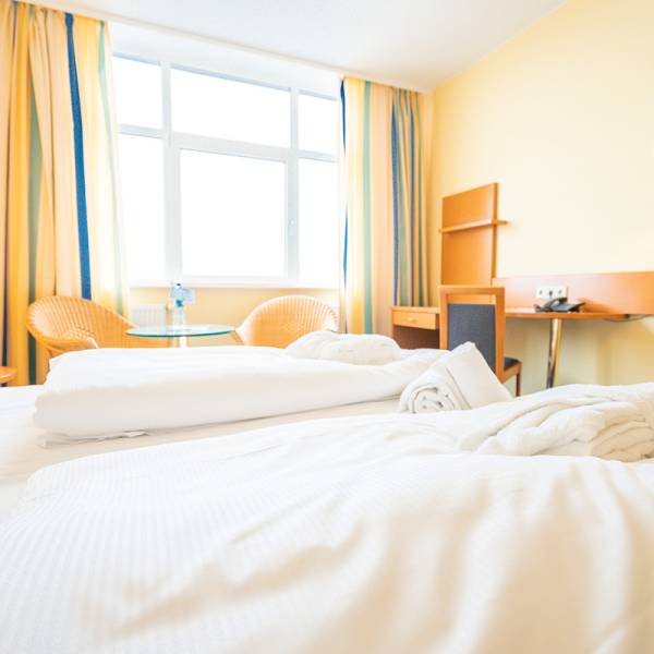 Double room at Arkona Strandhotel featuring a large bed, seating area with two wicker chairs, and a desk.