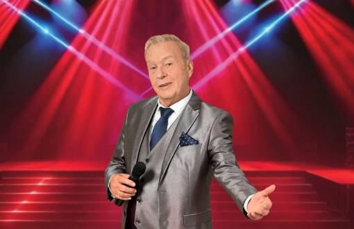 Eleganter Sänger im silbernen Anzug mit Mikrofon vor roter Lichtshow auf der Bühne beim Schlagerabend im Arkona Strandhotel