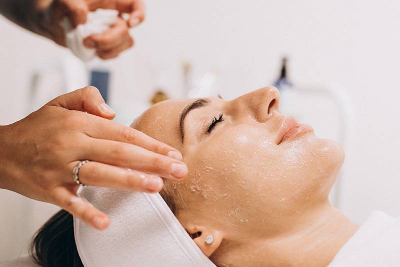Eine Frau mit geschlossenen Augen erhält im Arkona Strandhotel Rügen eine Gesichtsbehandlung mit Peeling im Rahmen der Biodroga Organic Pflege