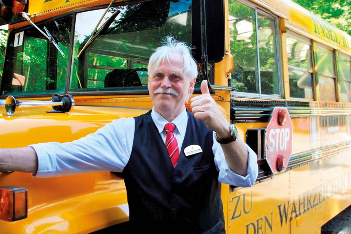 Ein Mann in Uniform lächelt in die Kamera, hält den Daumen nach oben und steht vor einem gelben Schulbus.