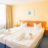 Ein ordentlich gemachtes Hotelbett in einem Hotelzimmer in gelben und blauen Farben gehalten.
