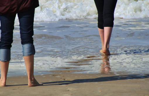 Zwei Personen laufen mit hochgekrempelten Hosen und barfuß ins Meer beim Kneippen im Urlaub im Arkona Strandhotel.