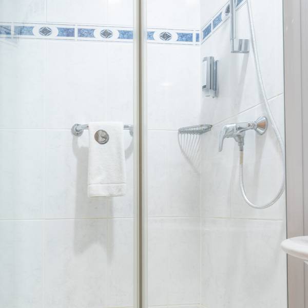 Bathroom at Arkona Strandhotel with a spacious shower, glass doors, and white tiles.