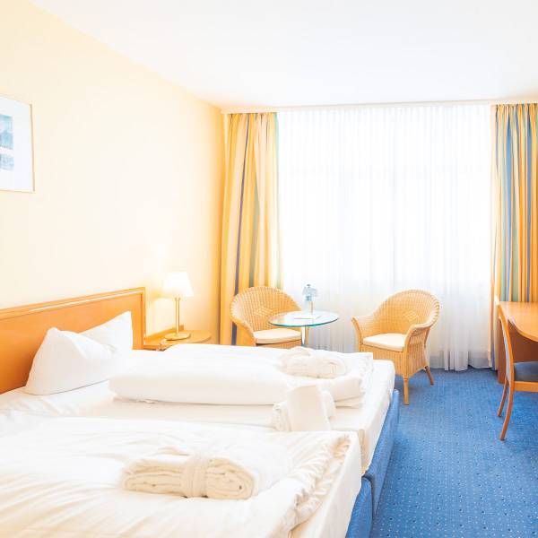 Double room on the ground floor of Arkona Strandhotel with a view of the bed, seating area, and window with curtains.