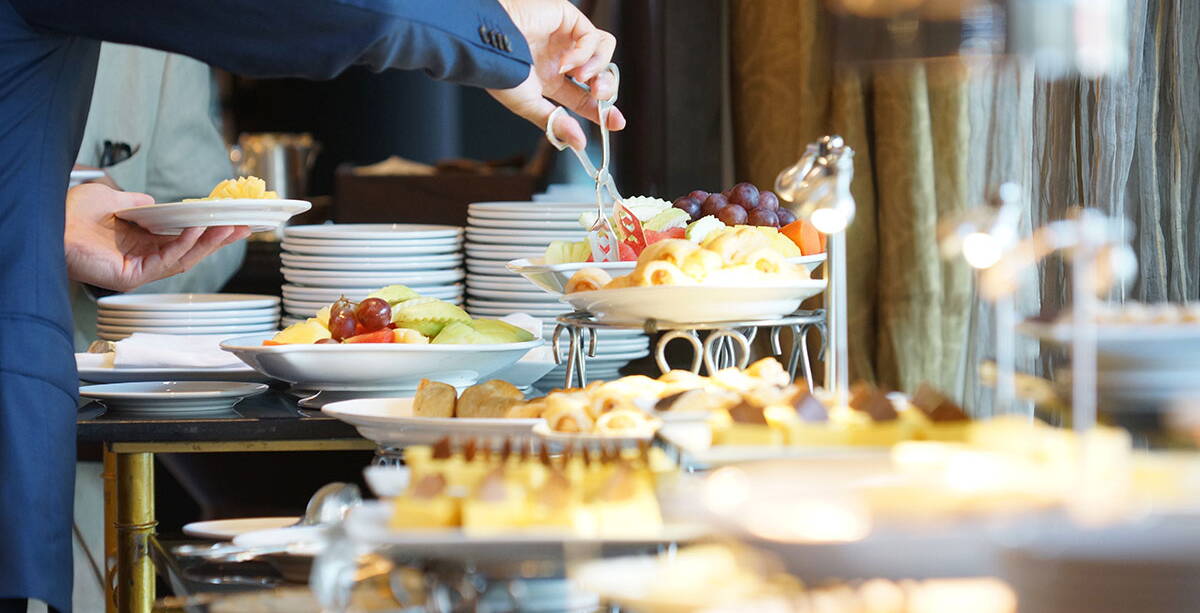 Ein Gast bedient sich am reichlich ausgestatteten Frühstücksbuffet mit Obst und Gebäck.