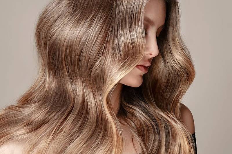Eine voluminöse Wellenfrisur an den langen Haaren einer blonden Frau.