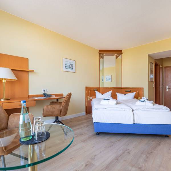 Double room at Arkona Strandhotel Binz with bed, desk, sitting area, and large window with sea view.