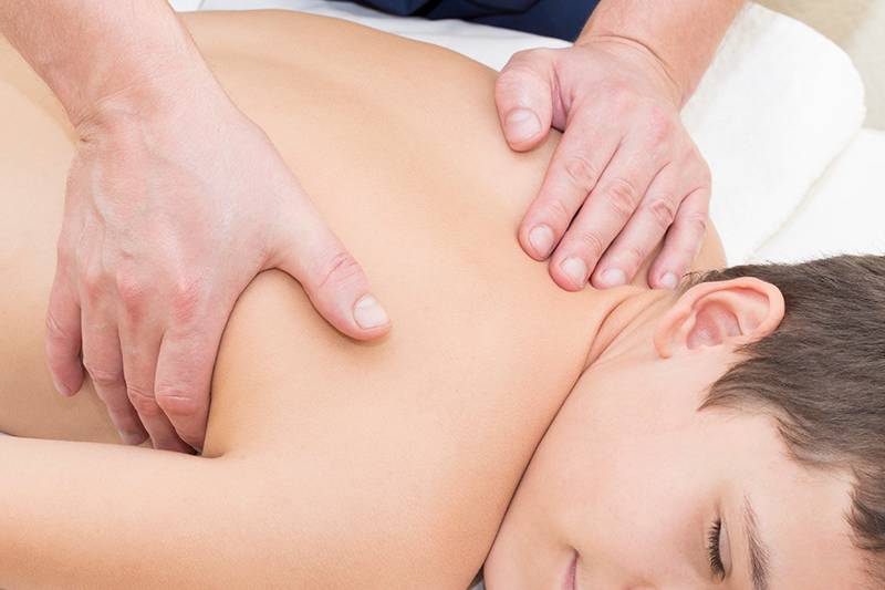 Ein lächelnder Junge liegt entspannt auf einer Massageliege im Arkona Strandhotel Rügen, während eine Rückenmassage durchgeführt wird