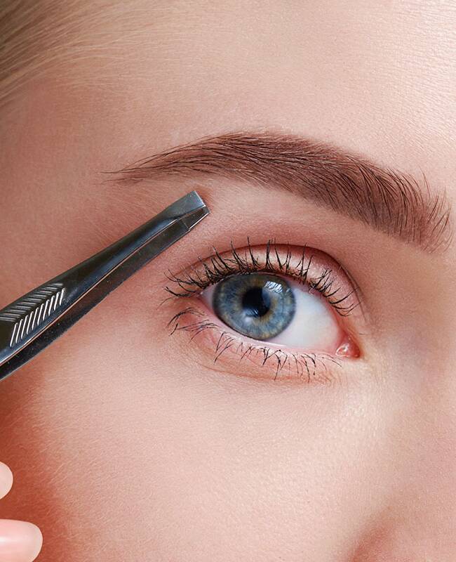 Nahaufnahme der blauen Augen einer Frau mit einer Pinzette neben den Augenbrauen.