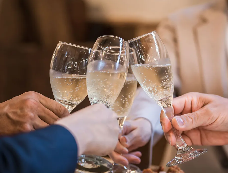 People clinking glasses of champagne, celebrating in a convivial atmosphere with food in the background.