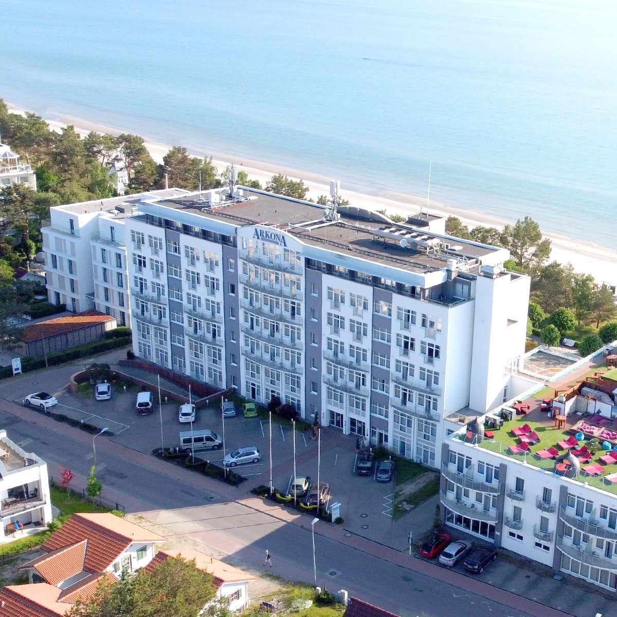 Aufnahme aus der Luft des Arkona Strandhotel direkt am Meer, im Hintergrund Bäume und der Strand.