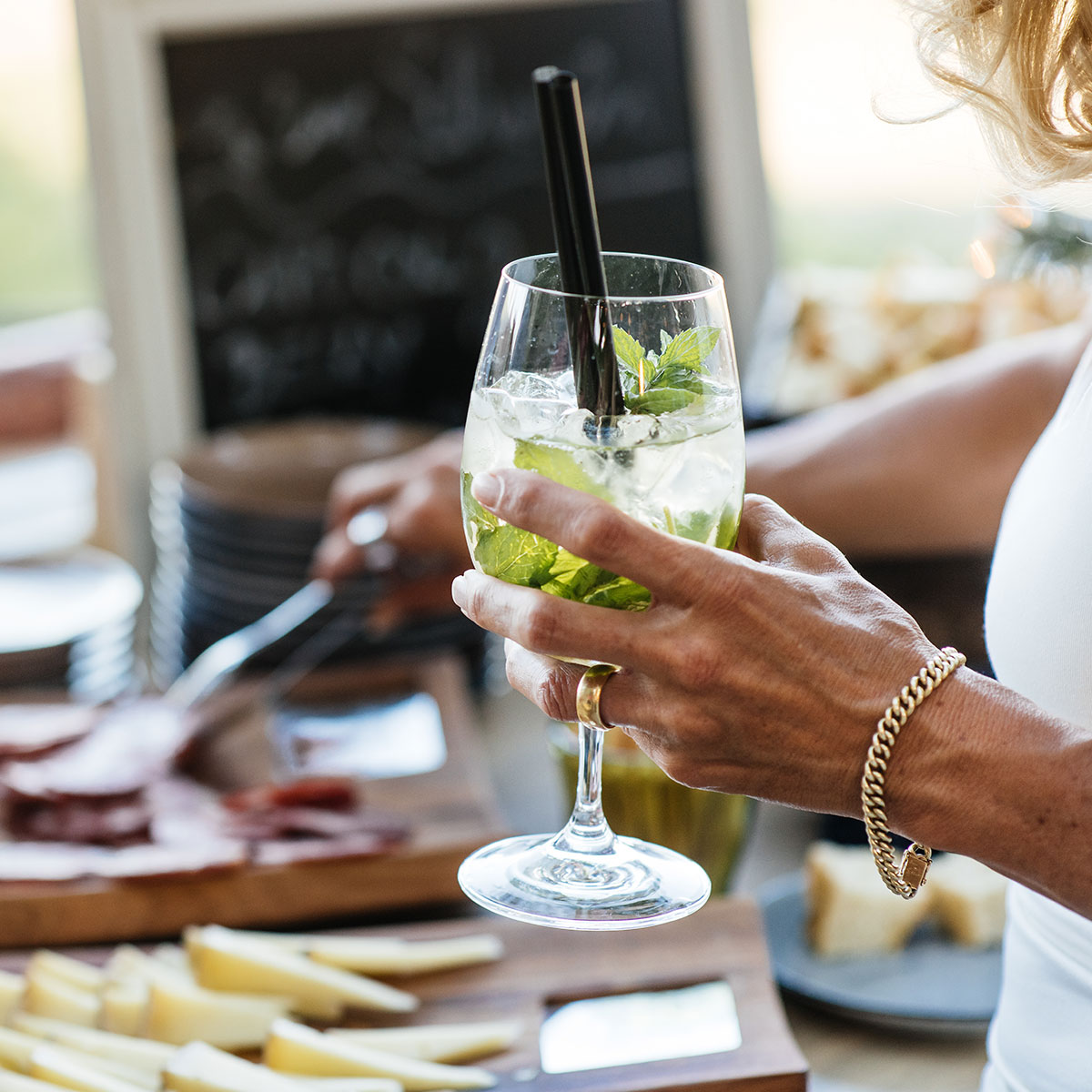 Detailaufnahme einer Frau, die einen Cocktail in der Hand hält und sich etwas vom Buffett nimmt.
