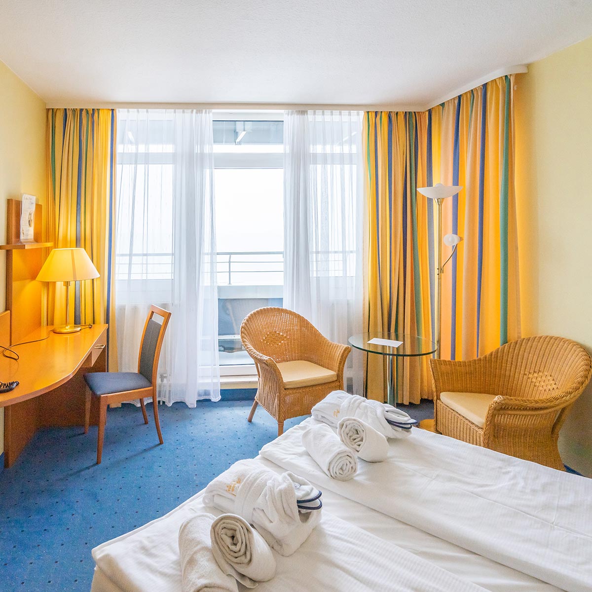 Ein großes Fenster in einem Hotelzimmer mit gelb gestreiften Vorhängen und blauem Teppichboden.