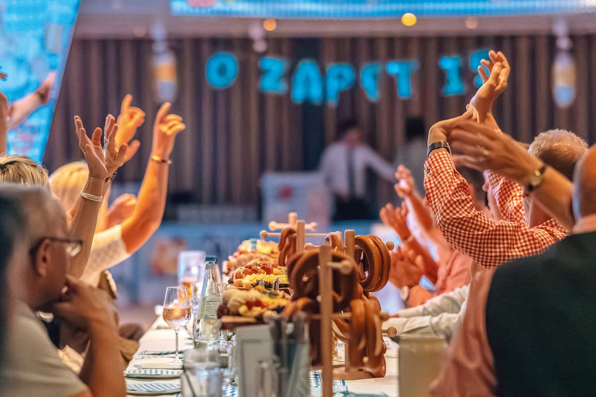 Gäste feiern mit erhobenen Armen beim 4. Binzer Oktoberfest mit traditioneller Kulinarik und festlicher Dekoration im Arkona Strandhotel.