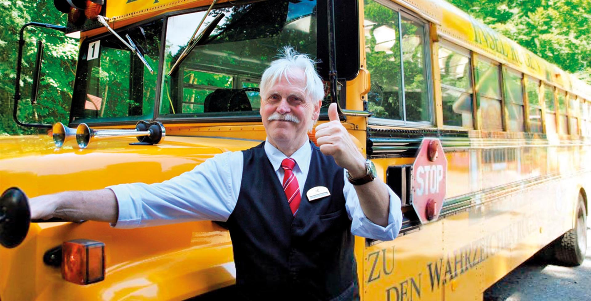 Ein Mann in Uniform lächelt in die Kamera, hält den Daumen nach oben und steht vor einem gelben Schulbus.