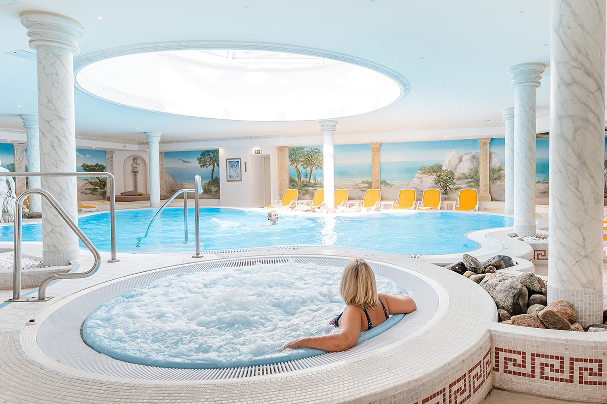 Eine Frau sitzt entspannt im Whirlpool im Wellnessbereich des Hotels, im Hintergrund ein großer Pool.
