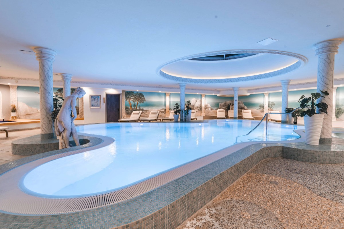 Large indoor pool in the wellness area at Arkona Strandhotel Binz on Rügen with columns, sculpture and loungers