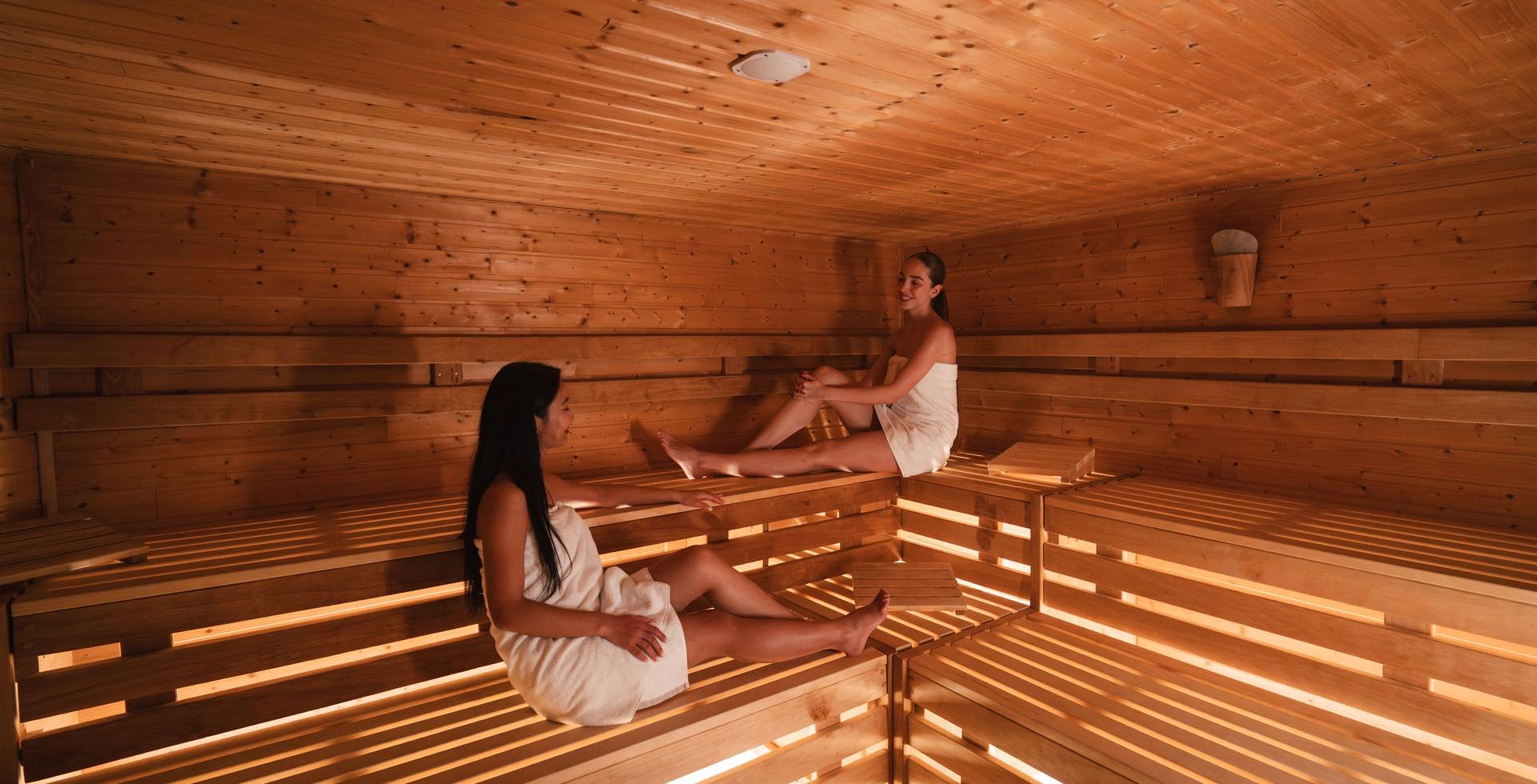 Two women sitting in the sauna at Arkona Strandhotel Binz on Rügen on wooden benches made of light wood